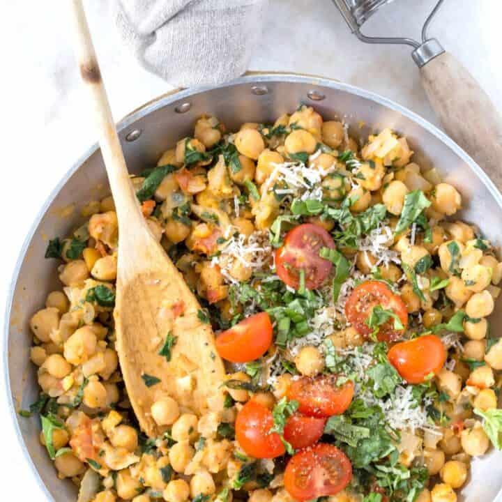 An aluminum skillet filled with cooked chickpeas and spinach.