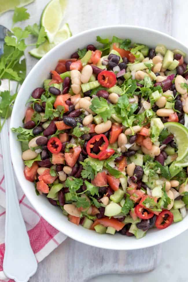 white bowl filled with three bean salad. Red and white dish towel next to the bowl with a serving spoon.