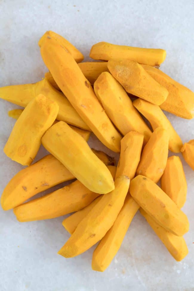 A pile of peeled fresh turmeric sits on a white cutting board for making a lemon ginger turmeric shot.