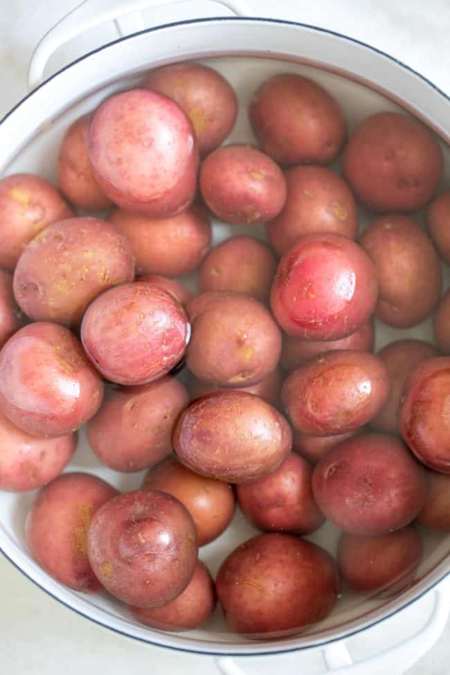 A white pot filled with baby red skin potatoes in water