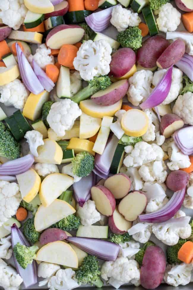 Cooking sheet filled with raw cauliflower, zucchini, yellow squash, red onion, carrots and broccoli