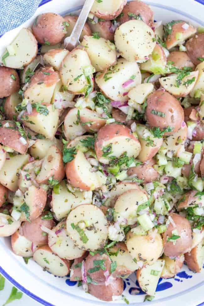 A white bowl filled with red potato salad and fresh herbs.