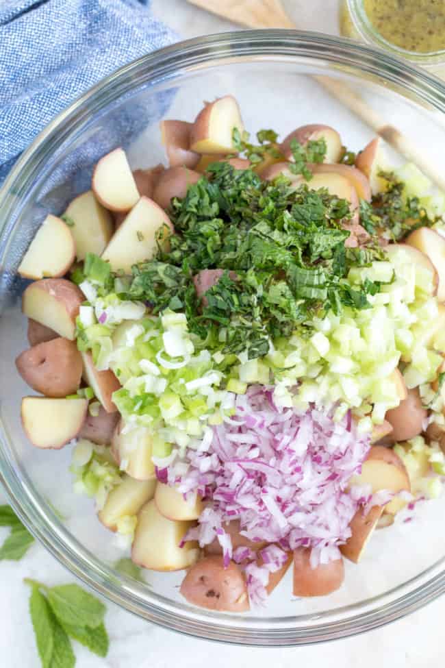 A clear mixing bowl filled with chopped vegetables and herbs.