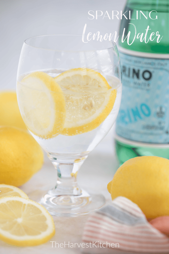 A clear drinking glass filled with sparkling water with slices of citrus. A bottle of sparkling water sits next to the glass.