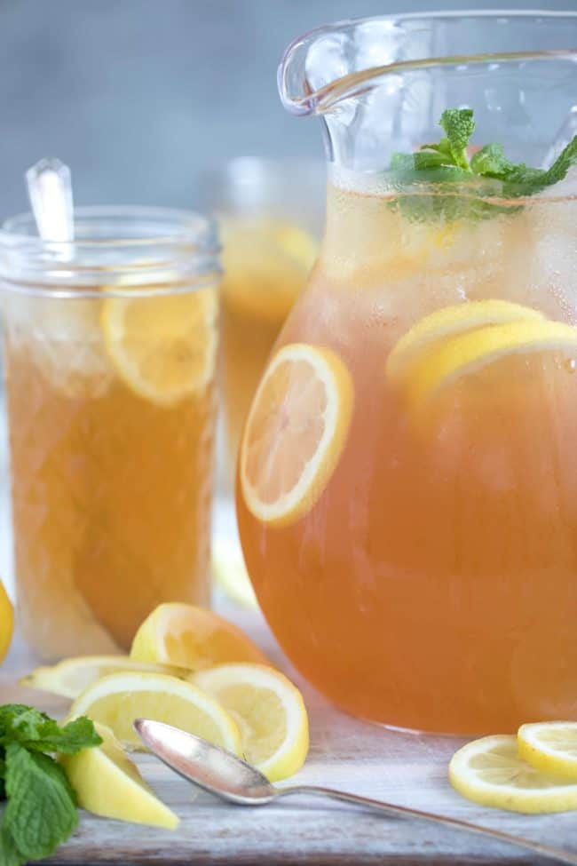 A clear glass pitcher filled with Arnold Palmer tea. A glass of iced tea lemonade sits next to the pitcher.