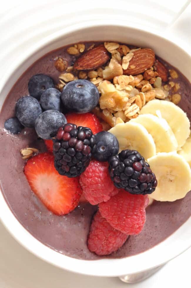 A white bowl filled with acai smoothie with fruit and granola.