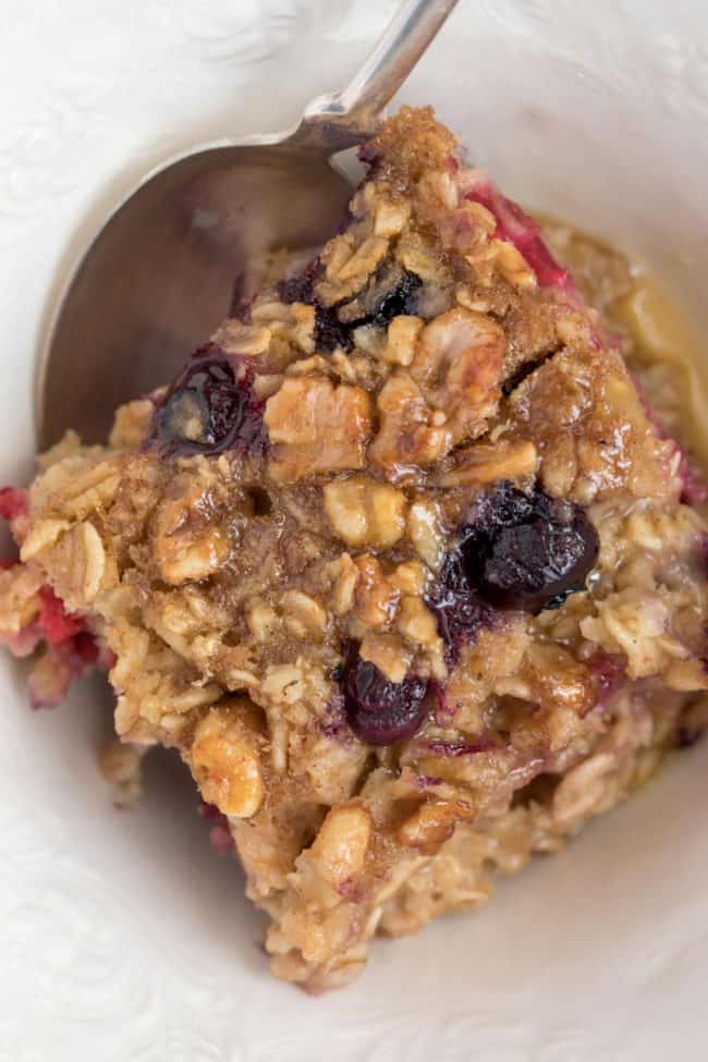 A white bowl with a serving of berry baked oatmeal. A spoon rests in the bowl.