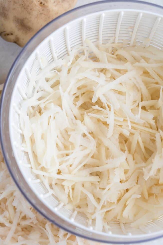 A salad spinner filled with shredded potatoes.