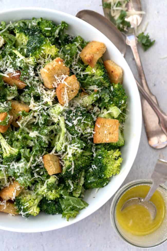 A white bowl filled with salad. Two spoons sit next to the bowl.