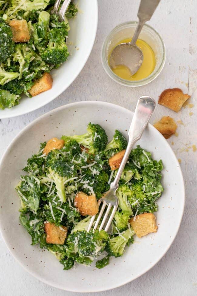 White plates with broccoli and kale salad. Forks sit on the plates.