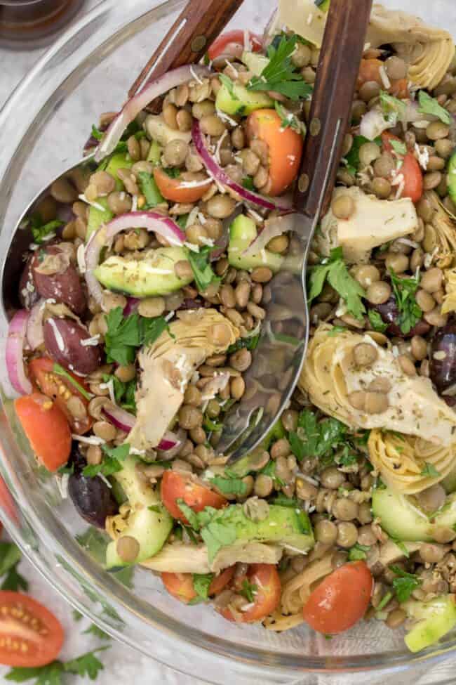 A clear glass bowl of Mediterranean lentil salad.