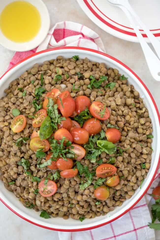 A bowl with cooked lentils and tomatoes and parsley.