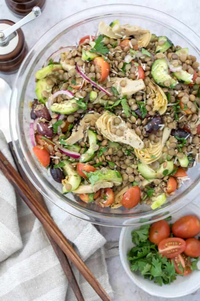 A glass bowl filled with chopped vegetables and legumes.