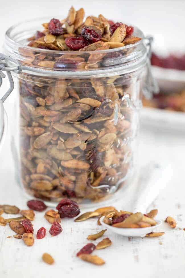 A glass mason jar filled with roasted pumpkin seeds and dried cranberries