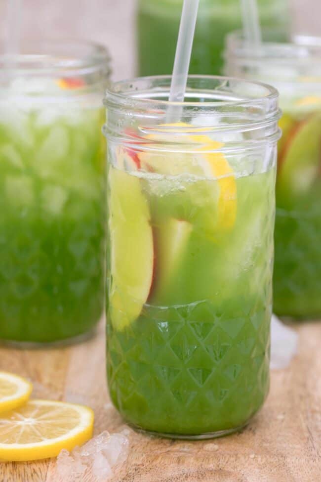 Three clear drinking glasses filled with green juice and slices of apple and lemon.