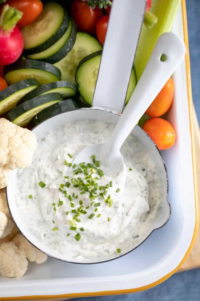 A white tray filled with an assortment of vegetables next to a white bowl of ranch dip.