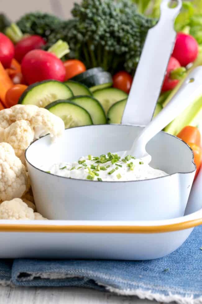 A white tray filled with an assortment of vegetables with a white bowl filled with Greek yogurt ranch dip.