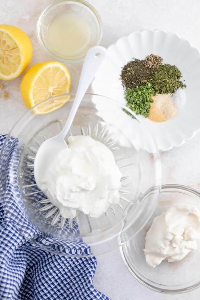 Clear glass bowls filled with yogurt, mayonnaise, seasoning and lemon juice to make homemade ranch dip.