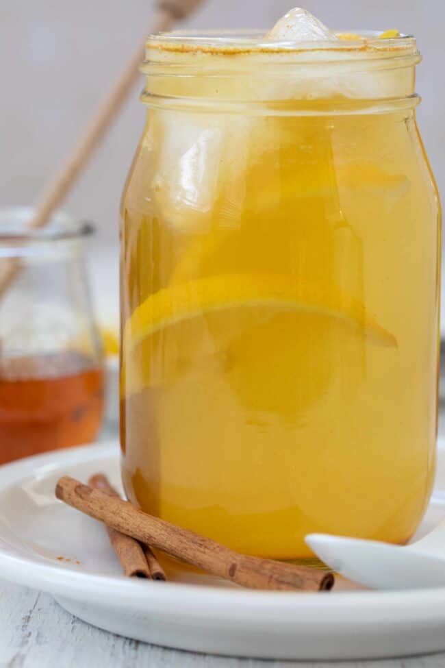 A clear glass mason jar filled with ACV and lemon juice, ice and orange slices.