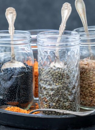 Four clear glass jars filled with different types of dried lentils