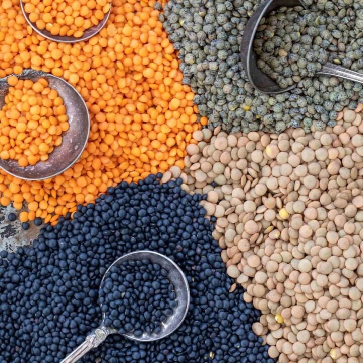 A black tray filled with piles of different types of dried lentils. Four spoons rest in the lentils.