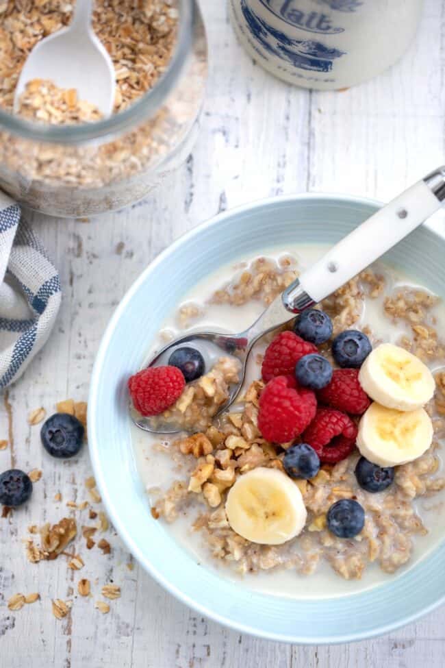 A light blue bowl filled with cooked instant oatmeal and sliced bananas and berries. 