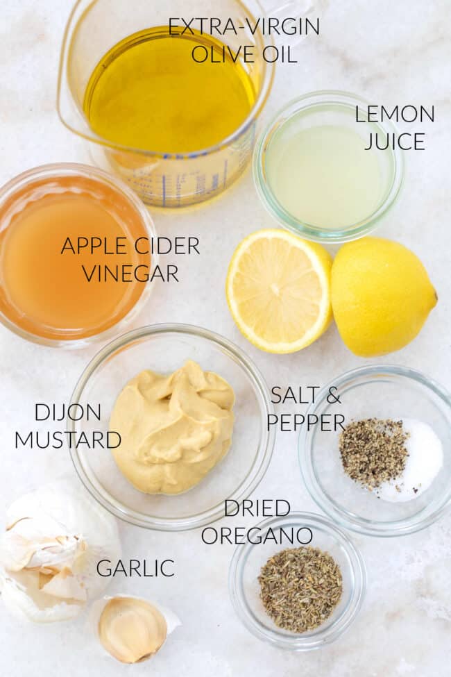 Several small glass mixing bowls filled with lemon juice, Dijon mustard, olive oil and spices. 