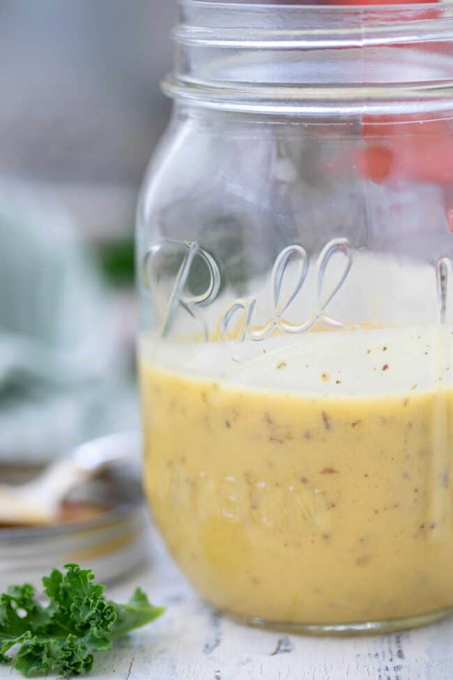 clear mason jar with homemade apple cider vinegar salad dressing. A spoon rests in the mason jar lid.