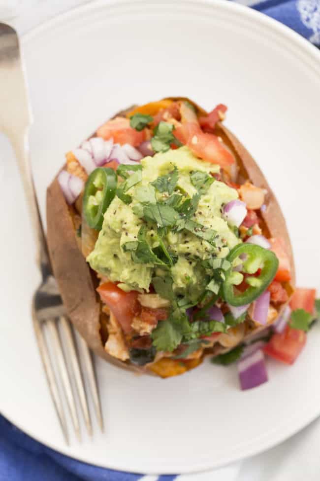 Mexican spuds filled with chicken fajitas, guacamole and pico de gallon on a white plate with a fork.