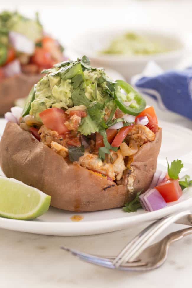 A baked sweet potato stuffed with chicken fajitas on a white plate.