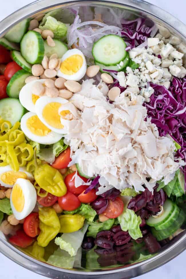 A mixing bowl filled with mixed greens, turkey lunch meat and hard boiled eggs.