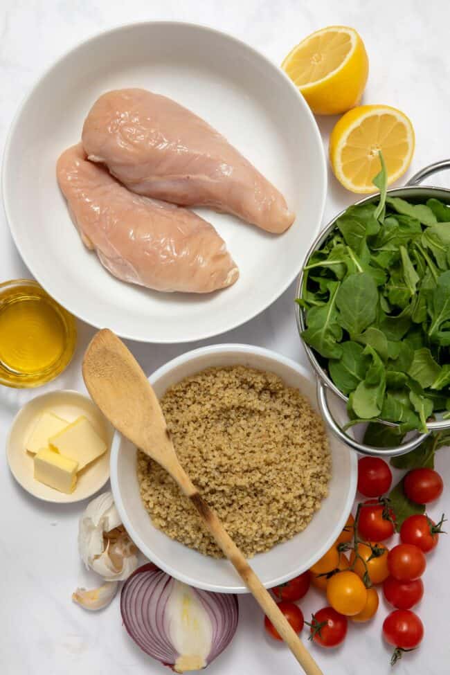 Raw chicken in a white bowl, cooked quinoa in a white bowl, next to a bowl of spinach -(ingredients for quinoa chicken bowl)