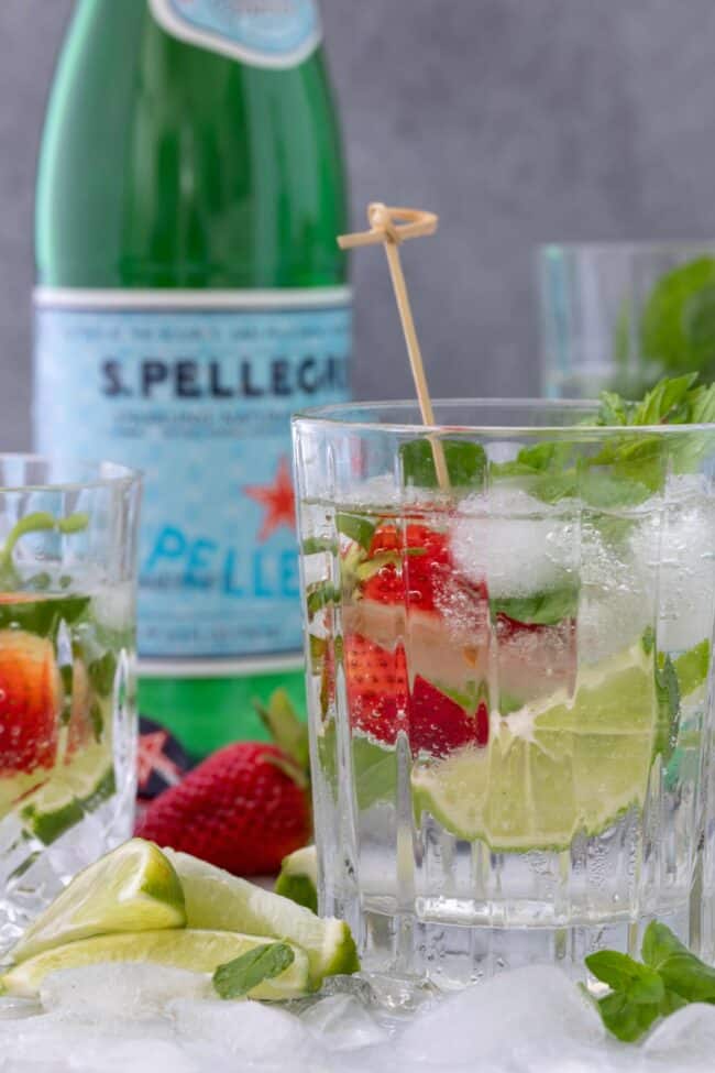 A clear drinking glass filled with sparkling water. A green bottle of sparkling water sits next to the glass.