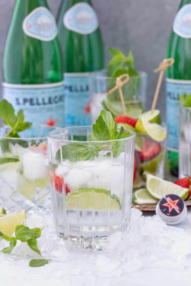 A clear glass filled with sparkling water. Several bottles of sparkling water sit behind the glass.