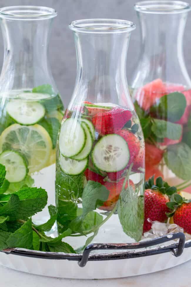 Clear glass carafes filled with water, cucumber and fresh herbs.