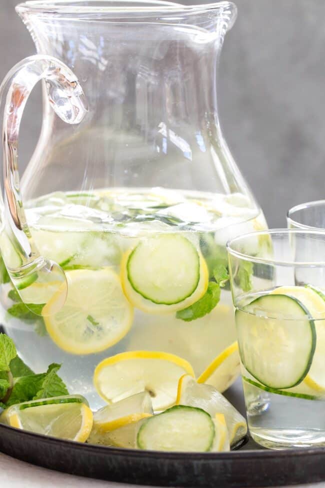 A clear glass pitcher filled with H2O and sliced fruit and herbs. 