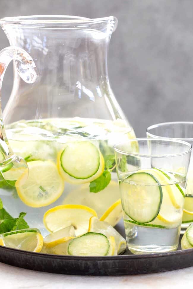 A clear glass pitcher of water with cucumber and lemon slices.