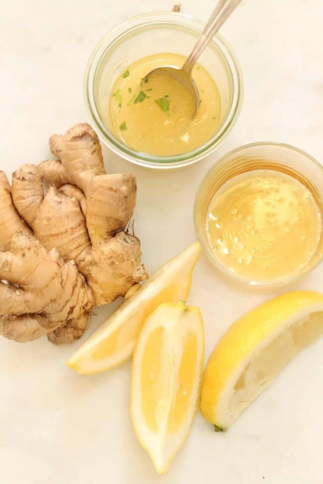 A jar filled with homemade salad dressing. Fresh ginger root and lemon wedges sit next to the jar.