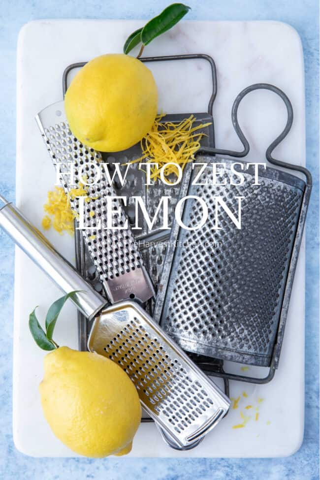 Two lemons on a white cutting board with a zester.