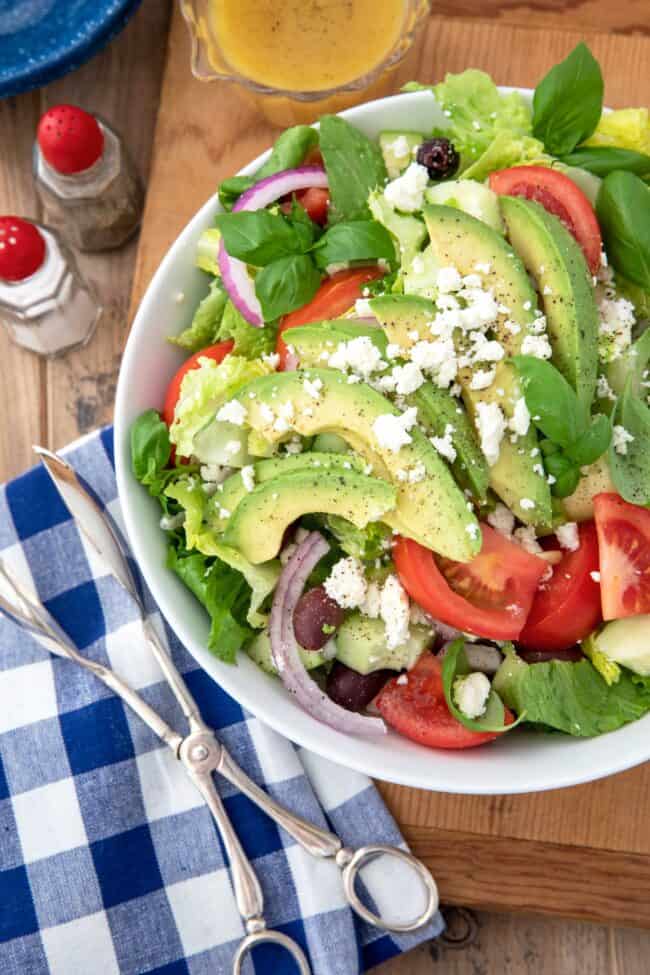 A white bowl of Romaine lettuce salad with avocado, kalamata olives and tomatoes.
