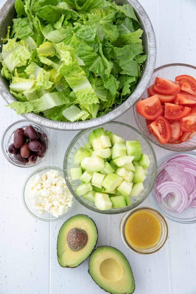 Glass bowls of Romaine lettuce, chopped tomatoes, cucumber, kalamata olives and avocado