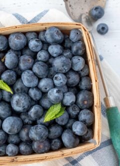 a wooden fruit basket filled with blueberries. A spoon sits next to the basket.
