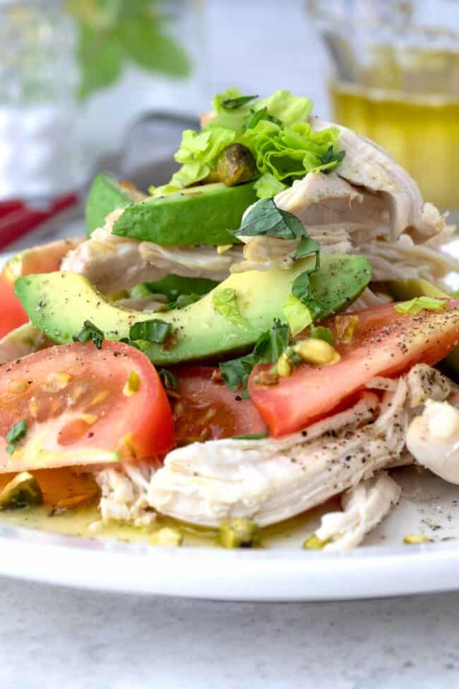 A white plate filled with avocado and tomato salad with chicken.