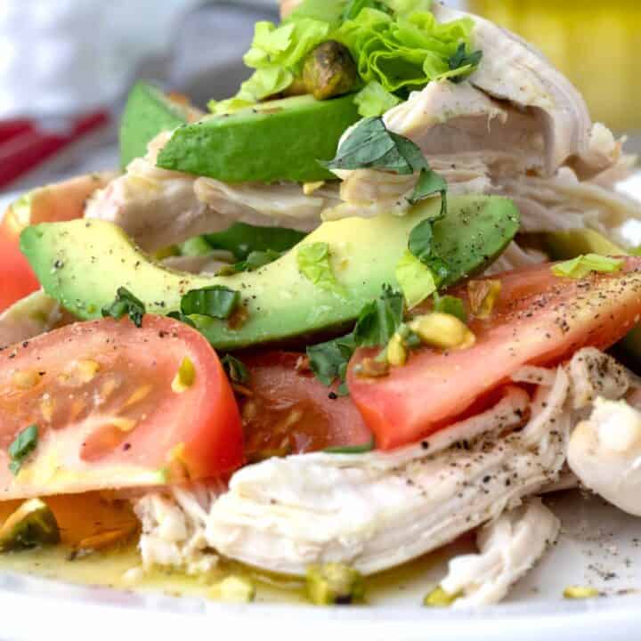 A white plate filled with avocado and tomato salad with chicken.