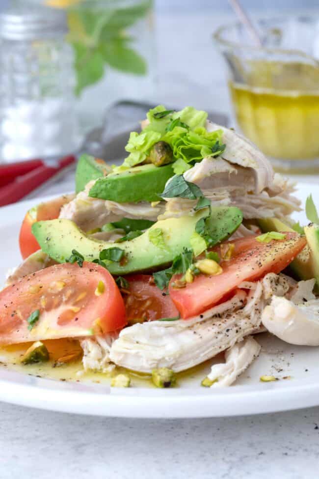 A white plate of avocado tomato salad with chicken.