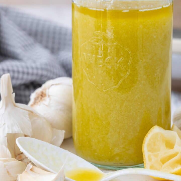 A clear glass jar of garlic oil. A white spoon rests next to the jar.