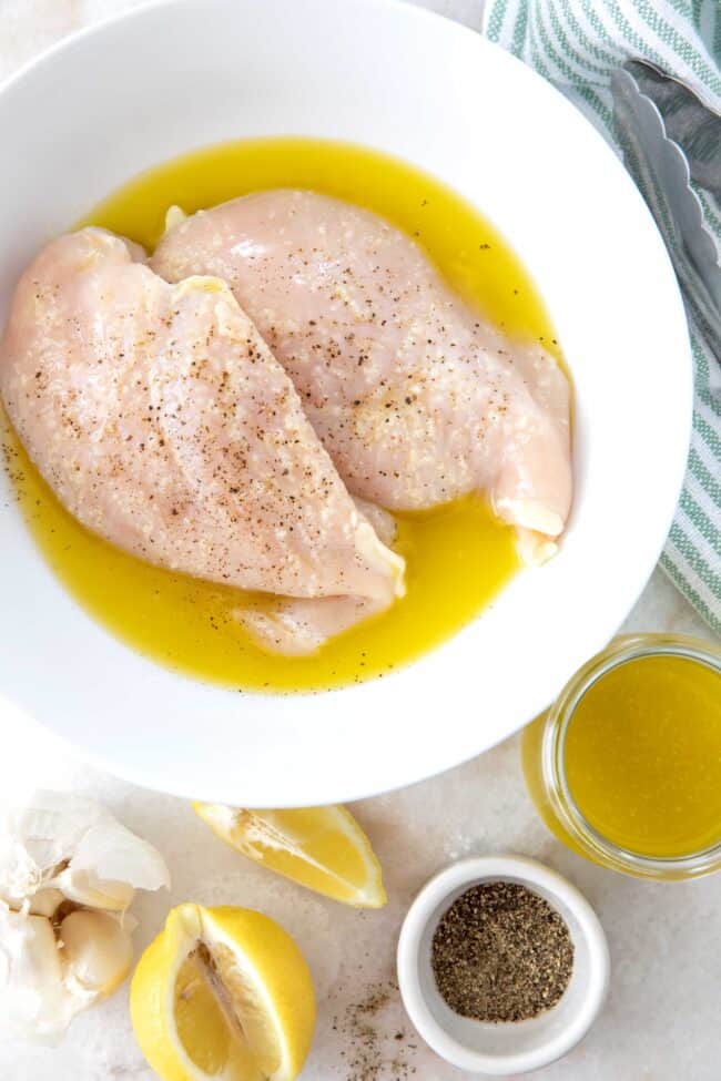 A white bowl with two chicken breasts marinating in a citrus marinade.