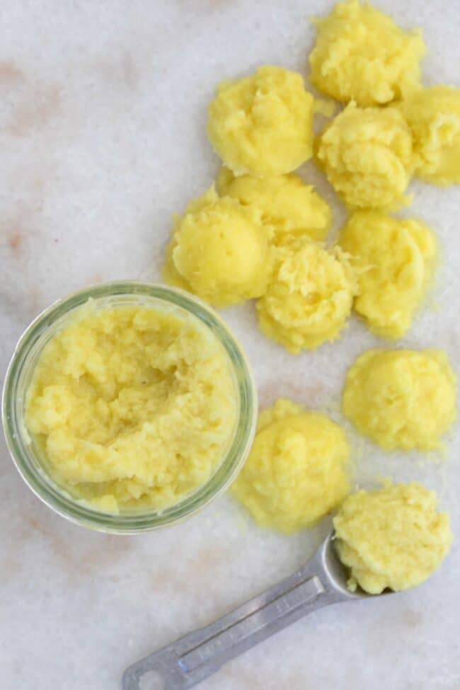 A teaspoon on a marble board next to frozen tablespoon scoops of ginger paste.