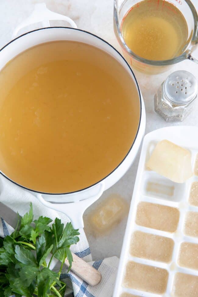 A white pot of chicken broth with ice cube tray filled with frozen broth