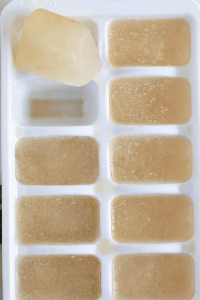 A white ice cube tray filled with frozen chicken broth ice cubes.